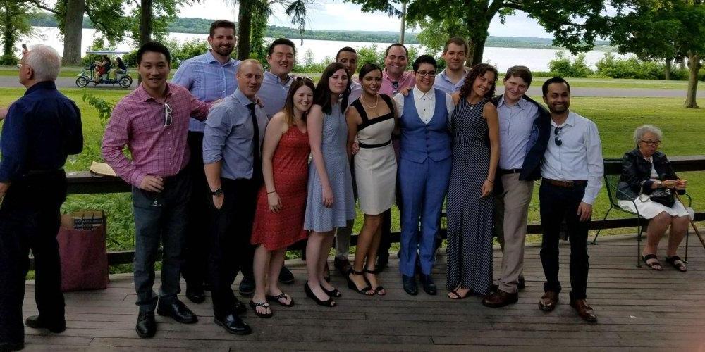 Image of a diverse group of young adults, dressed for a summer cocktail party, posing for a group photo on an outdoor deck