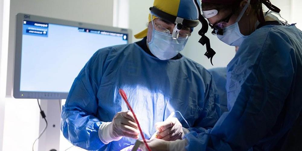 上州的谢拉德·塔图姆, 医学博士(右), 是一个前往乌克兰治疗严重战争创伤的面部和整形外科医生团队的成员之一吗. 他的手术帽是乌克兰国旗的颜色.